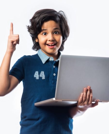 Asian Indian school kid holding and using laptop while standing against white background